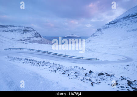 Snow covered road winding down between mountains near Nordradalur on the Island of Streymoy, Faroe Islands, Denmark, Europe. Win Stock Photo