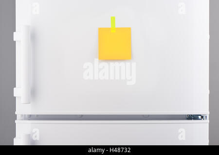 Blank yellow paper note attached with yellow sticker on white refrigerator door Stock Photo