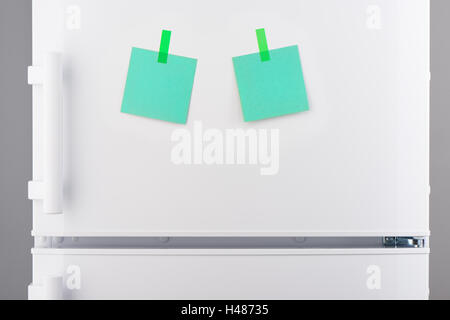 Two blank green paper notes attached with green stickers on white refrigerator door Stock Photo