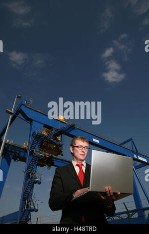 Businessman, seriously, laptop, half portrait, container terminal, loading engine, logistics, container port, container terminal, business, trade, people, man, glasses, suit, stand, work, communicate thoughtful, intently, data entry, planning, coordination, control, data transmission, e-mail, Internet, Internet connection, communication, WLAN, without cable, notebook computer, computer, portable, mobility, flexibility, crane, Verladekran, transport, cargo, goods, goods traffic, outside, cloudy sky, Stock Photo