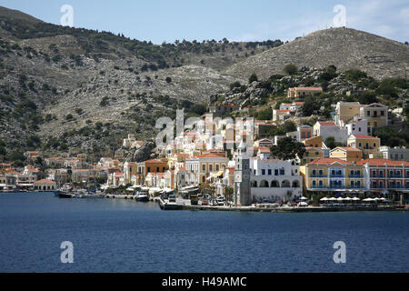 Greece, Dodekanes, Rhodes, island, Symi, harbour place Gialos, town view, promenade, clock tower, hill, sea, coast, seashore, coastal place, local view, Simi, town, island capital, mountains, Symi town, houses, harbour, tower, architecture, boots, ships, bank promenade, harbour promenade, street cafe, place of interest, holiday resort, Stock Photo