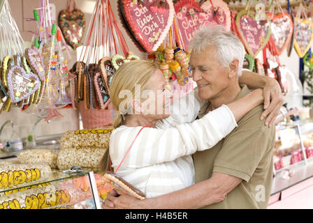 Funfair, senior couple, happy, eye contact, embracing, gingerbread heart, half portrait, side view, Stock Photo