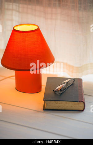 red desk lamp, book and glasses on window sill. copy space Stock Photo