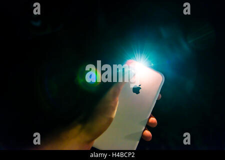 Hand holding Apple iPhone with flashlight feature, in the dark Stock Photo