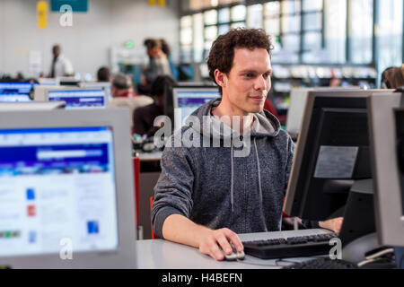 Smiling student using a computer in a library to perform some researches for high school Stock Photo