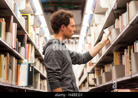 Young male student selecting a book from a library shelf, high school Stock Photo