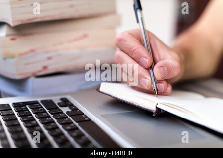 Young traveler writing down journey stories in a notebook with a laptop and books in the background Stock Photo