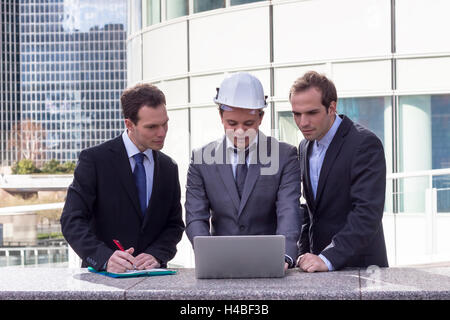 Business team with architect and engineer analyzing project on laptop with office buildings in background Stock Photo