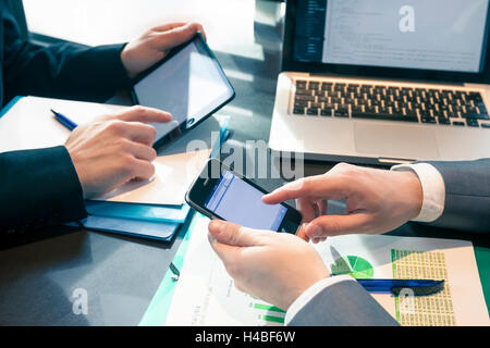 Businessmen at meeting presenting charts on smartphone, tablet and laptop Stock Photo