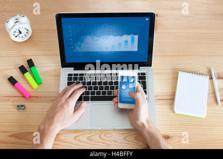Businessman working online on laptop and smartphone from home with wooden desktop, top-view Stock Photo