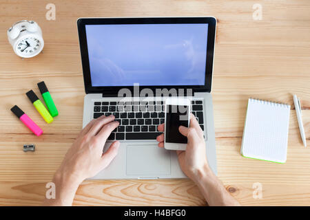 Young adult working with mobile phone and laptop, top-view Stock Photo
