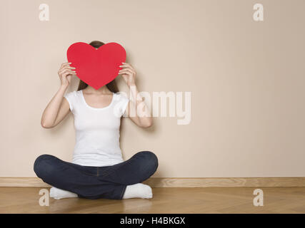 Woman, young, seated, face hidden behind a heart, Stock Photo