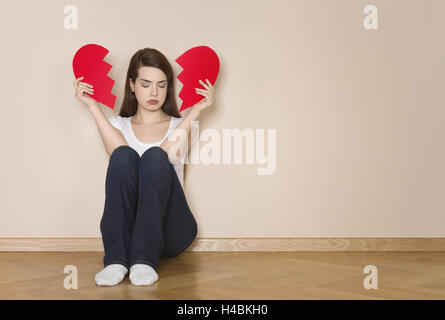 Woman holds divided heart in her hands, sits sadly on the floor, Stock Photo