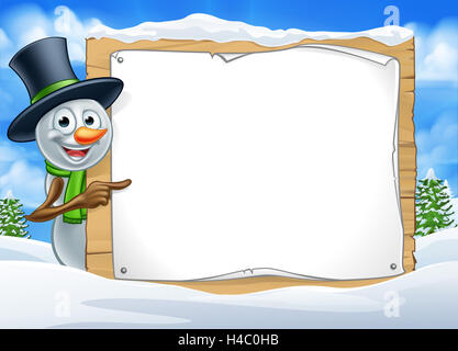 A happy Christmas snowman cartoon character in a winter scene peeking around pointing at a sign Stock Photo
