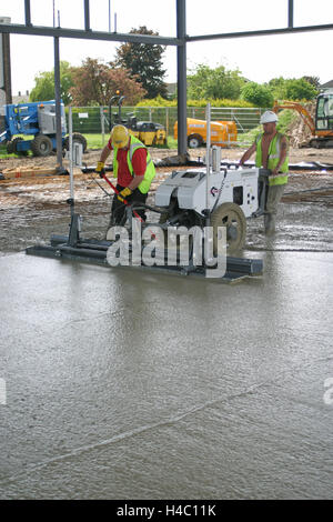 Workmen use a computer controlled, laser leveled screeding machine to create a smooth concrete floor Stock Photo