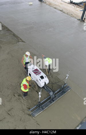High level view of workmen using a computer controlled, laser leveled screeding machine to create a smooth concrete floor Stock Photo