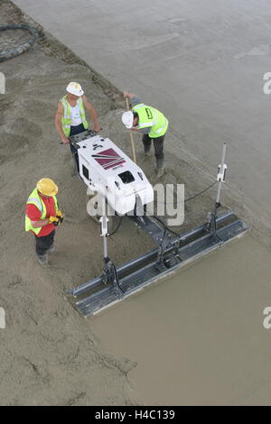 High level view of workmen using a computer controlled, laser leveled screeding machine to create a smooth concrete floor Stock Photo