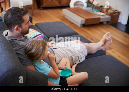 Father And Daughter Sitting On Sofa Watching TV Together Stock Photo