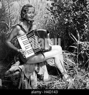 Eine junge Frau sitzt im sommerlichen Schilf mit einem Akkordeon, Deutschland 1930er Jahre. A young woman sitting in the reed on a shore with her accordion, Germany 1930s. Stock Photo