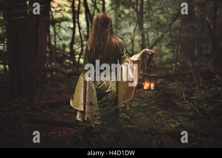 Mysterious woman walking in fairy forest with a lantern. Fantasy Stock Photo