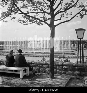Ein Paar sitzt auf einer Bank im Grugapark in Essen und schaut sich die Wasserspiele an, Deutschland 1930er Jahre. A couple sitting on a bench at Essen Grugapark gardens watching trick fountains, Germany 1930s.