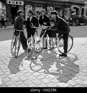 Vier junge Männer, drei davon mit einem Fahrrad, bei einer Unterhaltung auf der Straße in der Innenstadt von Cham, Deutschland 1930er Jahre. Four young men, three of them with a bicycle, talking on a street in the inner city of Cham, Germany 1930s. Stock Photo