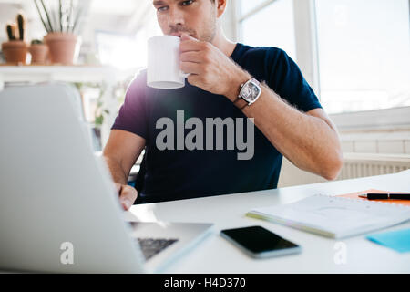 Businessman drinking coffee and working on laptop at workplace. Male executive working at his desk and drinking coffee. Stock Photo