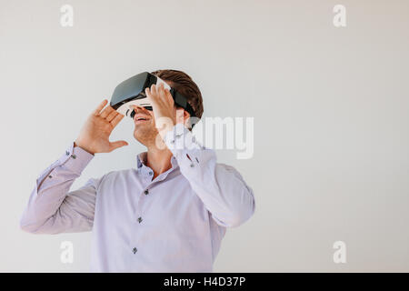 Happy young man using the virtual reality headset against grey background with copy space. Caucasian male model wearing VR goggl Stock Photo