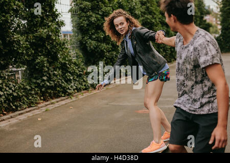 Teenage girl on a skateboard with support from her boyfriend. Woman skating on a basketball court with friend. Stock Photo