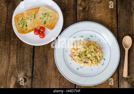 Scrambled eggs with chive and bacon, toast with herbs on wood table Stock Photo