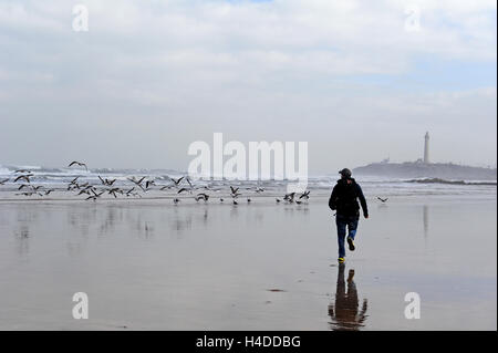 A boy running along the beach in Casablanca. The lighthouse can be seen in the background. Stock Photo