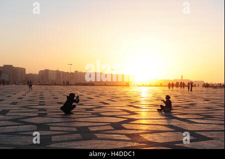 A girl takes a picture of her friend in the spacious forecourt of the Hassan II mosque at sunset Stock Photo