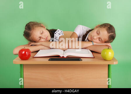 Two school girls sleeping on a stack of books at her desk isolated on green Stock Photo