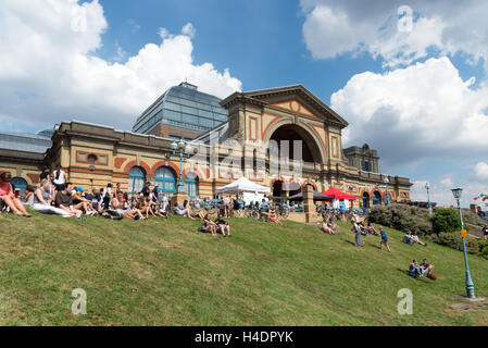 People sitting on grass outside Alexandra Palace during Alexandra Park Festival, Haringey, London, England, UK Stock Photo