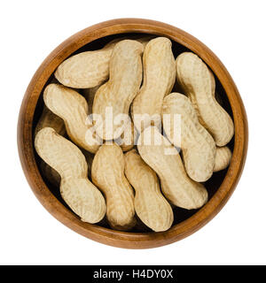 Peanuts with shell in wooden bowl over white, also called groundnut and goober. Dry roasted whole pods of Arachis hypogaea. Stock Photo