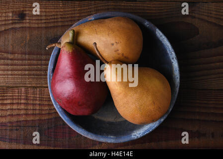 Top view of a group of Red and Bosc pears in a blue plate on a rustic wood table. Stock Photo