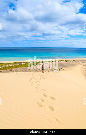 Footprints in sand with unidentified young woman walking down on a dune at Sotavento beach on Jandia peninsula, Fuerteventura, Canary Islands, Spain Stock Photo