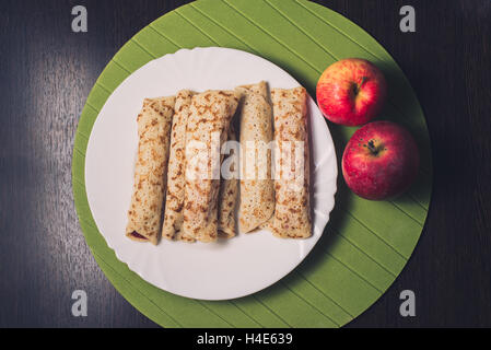 Roasted rolled pancakes on a white round plate and two apples near. Top view . Flat lay Stock Photo