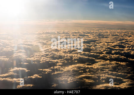 Sun flare above a dense layer of cloud viewed from an airplane flight in a travel and weather concept Stock Photo
