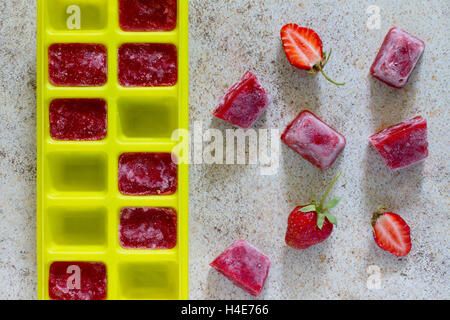 Ice made from strawberries for summer drinks with copy space on brown stone background. Stock Photo