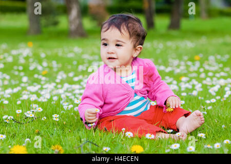 Cute chubby toddler sitting on the grass smiling exploring nature outdoors in the park Stock Photo