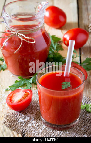 Glass of freshly squeezed tomato juice with green leaves on a wooden background, place for your text. Stock Photo