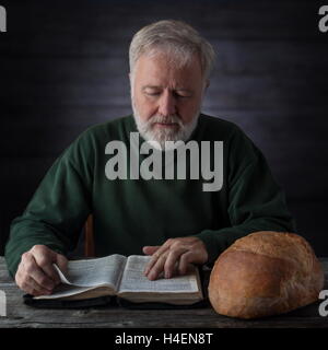 Senior pastor meditating and feeding on the Word of God not only with the daily bread next to him. Mat.4.4 Man shall not live by Stock Photo