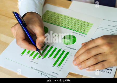 Businessman analyzing sustainable development opportunities charts at workspace. Hand holding a pen and green charts. Stock Photo