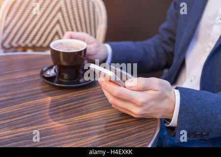 Young adult using mobile phone on restaurant terrace with coffee Stock Photo