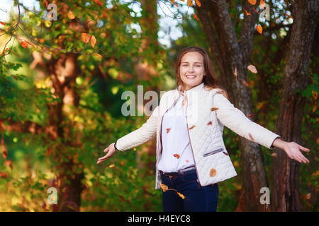 Young beautiful teenager girl tosses colorful autumn leaves in park Stock Photo
