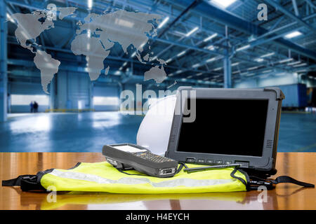 Rugged computers tablet and Bluetooth barcode scanner in front of modern warehouse with world map. Logistics concept. Stock Photo