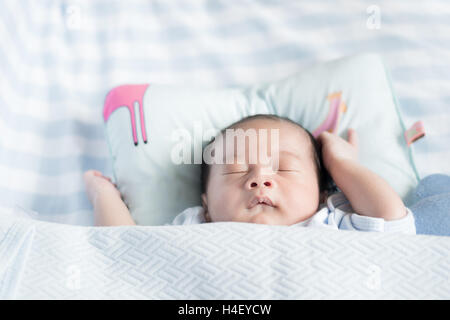 Asian newborn boy sleeping over his white bed covered with a blanket. One week old newborn boy. Stock Photo