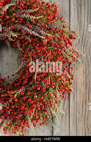 Autumn wreath on wooden wall cutout, tied with rosehip (Rosa canina), heather (Calluna vulgaris) Stock Photo