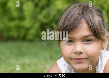 Closeup view of the slightly smiling face of little girl lying on the grass outdoors. Stock Photo